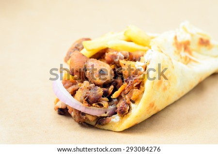 Traditional Greek pita gyros with meat, fried potatoes, tomato, onion and drink on brown Paper, Placed on blue Wooden Table board,