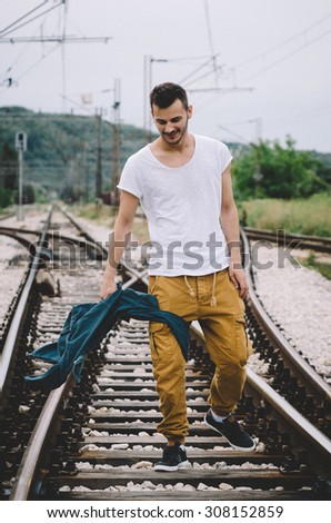 Young man throwing a jacket on the railroad. Vintage Instagram style effect, soft and selective focus, grain texture visible on maximum size
