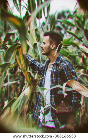 Young hipster man with vintage camera in a corn filed. Toy camera with distortion and Chromatic Aberrationstyle effect, soft focus, low light, grain texture visible on maximum size. Horizontal