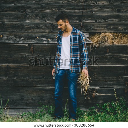 Young guy standing outside of old barn. Vintage retro style effect, soft and selective focus, low light, grain texture visible on maximum size.