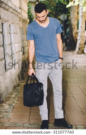 A stylish and handsome  man walking up a street in Belgrade, carrying a bag after work