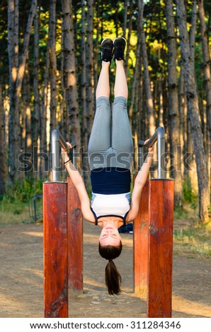 Young fitness woman hanging upside down during workout process in forest