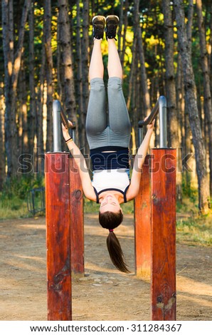 Young fitness woman hanging upside down in forest