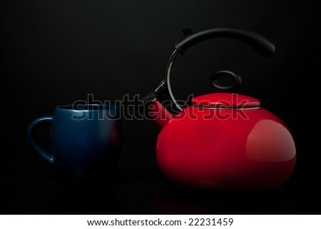 Red tea kettle and blue mug against black background.