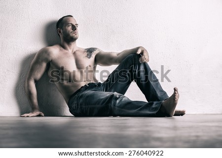 Man posing shirtless, leaning on white wall