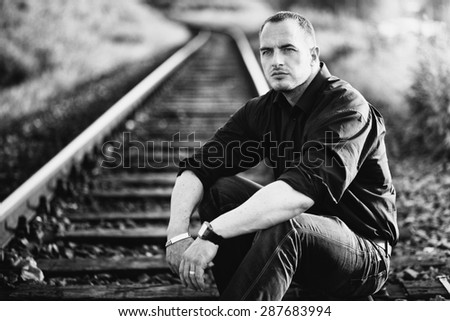 Man sitting on a rail track. Black and white photo with grain