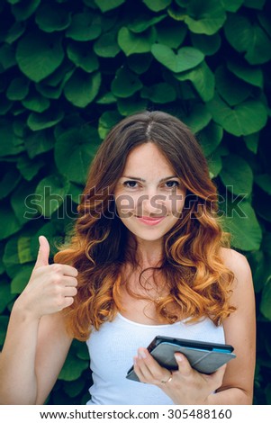 Young woman, against background of summer green park and green leaves with  a tablet.Young woman with a tablet in a park.
