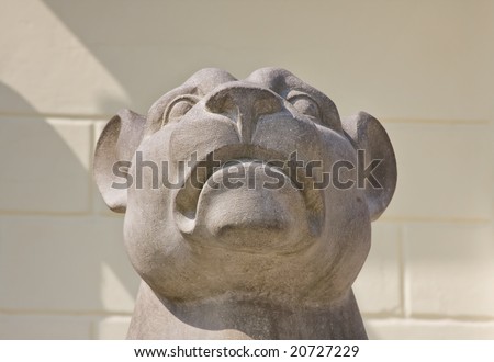 The top part of a sculpture of the lion covered by the sun, on a background of a light yellow wall