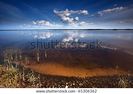 Quiet smooth surface of lake in windless solar weather with clouds reflected in water, Russia, Siberia