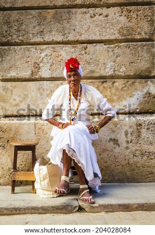 HAVANA, CUBA - DECEMBER 1, 2013:  Old black lady dressed in typical cuban clothes smoking a huge cuban cigar next to the Havana Cathedral.