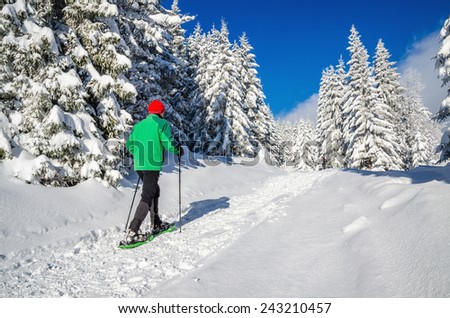 Athletic young man walking with snow shoes on winter hiking trail