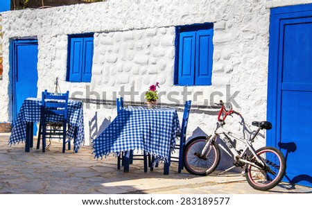 KALMNOS, GREECE- MAY 1, 2015: Typical Greek restaurant with blue tables and chairs and small bike parked