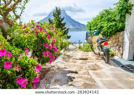 KALYMNOS, GREECE - MAY 01, 2015: Colorful flowers and scooter parked on read leading to sea on Greek Island, Greece