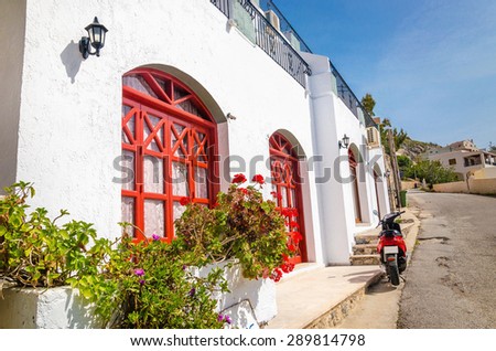 Red motorbike in front of typical Greek house with red doorframe and beautiful flowers, Greece