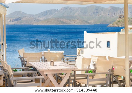 Iconic Greek restaurant with blue tablecloth and wooden chairs on a background of blue sea, Greece