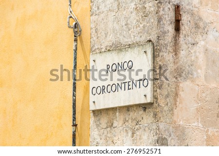 Marble plaque with the name of the road on yellow plastered wall with a part covered with marble in Palazzolo Acreide, Siracusa, Sicily, Italy