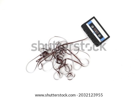 This shows a well known problem with the old fashioned compact cassettes: the tape used to come out, making the cassette useless. Vintage compact cassette tape on white background.