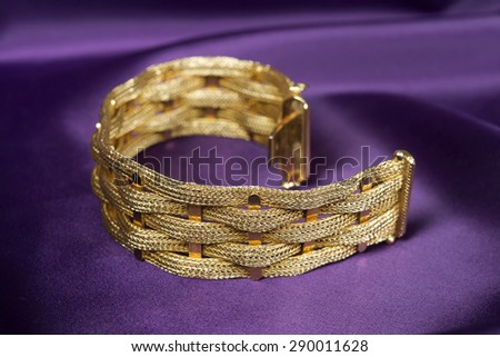 Gold bracelet isolated on purple satin background.