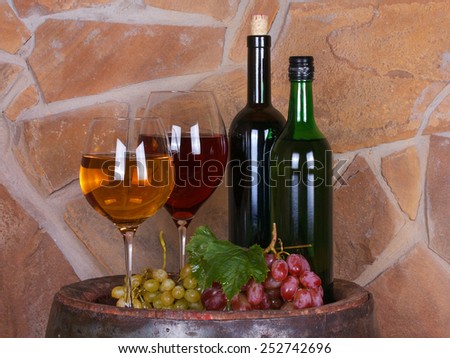Glasses and bottles of wine, cheese and grapes on old barrel with iron rings