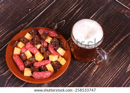 Glass of beer, cheese and smoked sausages plate