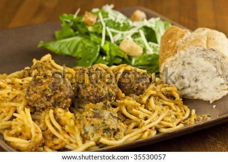 A meal of spaghetti and meatballs, with a side salad and bread