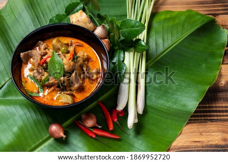 THAI BEEF RED CURRY. Thailand tradition red curry soup with beef  and coconut milk. Red Curry with ingredient in Black plate on  banana  leaf and woodden background.