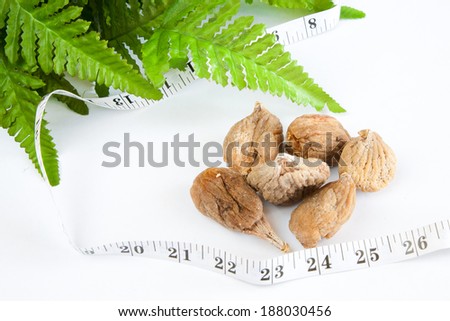 Dry figs, measure tape and green leaves on white background