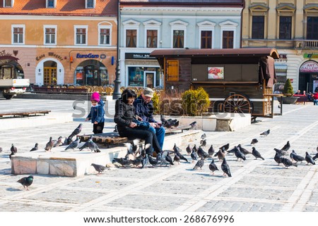 Brasov, Romania - March 25, 2015: People feeding the pigeons at the Piata Sfatului - Council Square in downtown of Brasov, Transylvania, Romania.