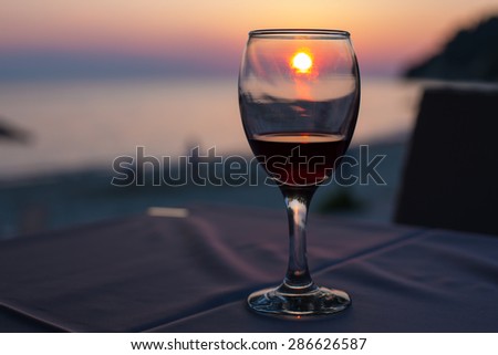 Sunset on beach reflected in glass of red wine, summertime vacation concept. Place for text