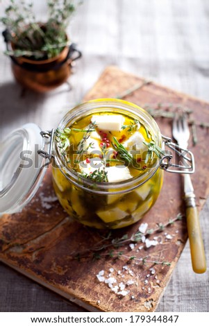 Cheese pieces with herbs and spices in olive oil in a glass jar standing on a vintage book