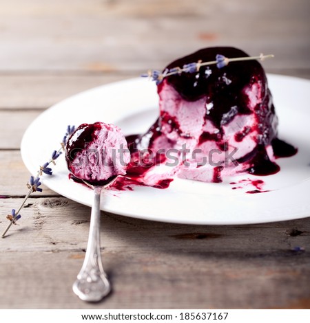 Berry ice cream with topping on a white plate with spoon on a wooden background