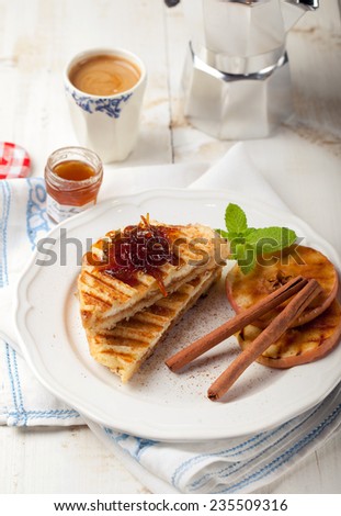 French toasts with orange marmalade, grilled apples and cinnamon sticks on a white plate with a cup of coffee. Traditional breakfast.