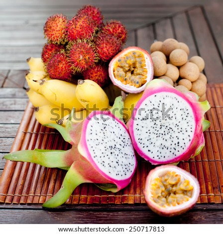 Assortment of tropical exotic fruits: dragon fruit, bananas, passion fruit, longan, rambutan on a wooden background