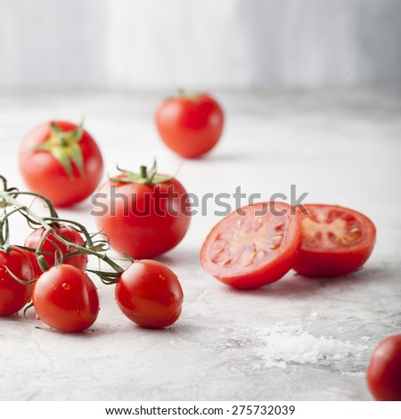Fresh grape tomatoes with sea salt  with a halved tomato in the foreground. Stone background