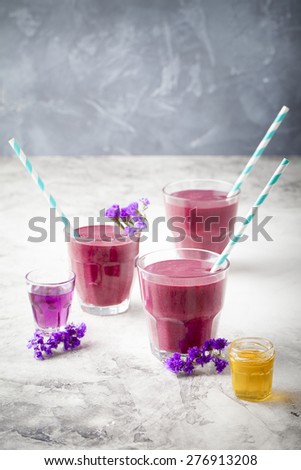 Blueberry, blackberry, honeysuckle, honeyberry smoothie with violet syrup and acai berry powder on a stone background. Copy space