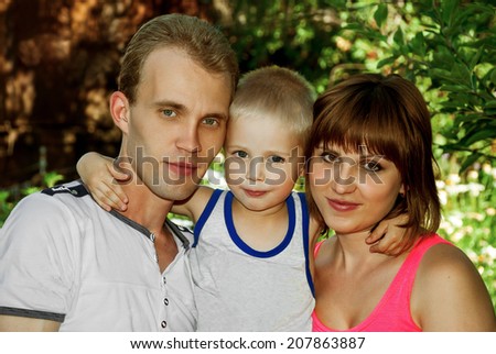 Mother and father and son hugging outdoors in a lush garden.