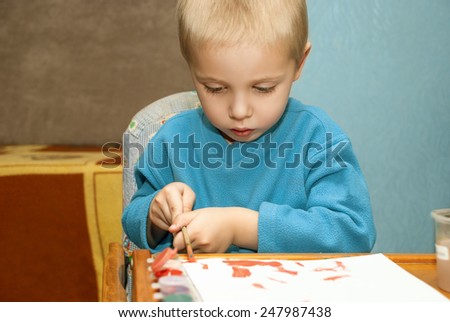 Cute little child painting with colorful paints in home.