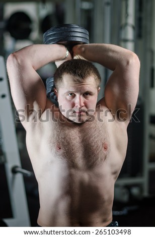 Young athlete at the gym doing exercise on triceps with a dumbbell sitting on the bench