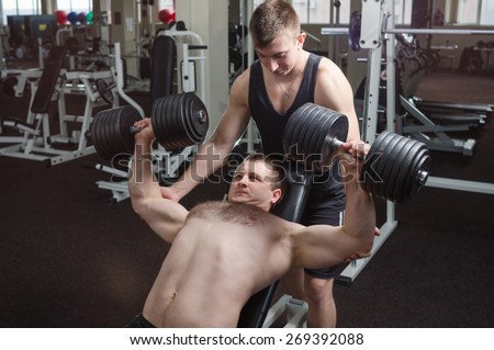 Young muscular man performs an exercise dumbbell bench press on an incline bench, with a partner that it insures.