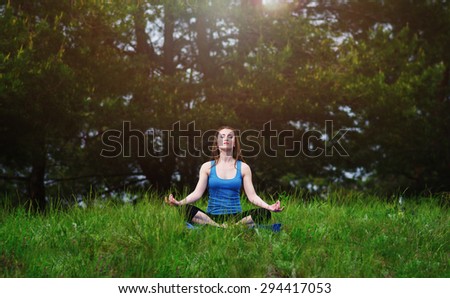 Young girl practicing yoga in nature in the woods on a background of green trees and grass.Woman covers a ray of sunshine at sunset