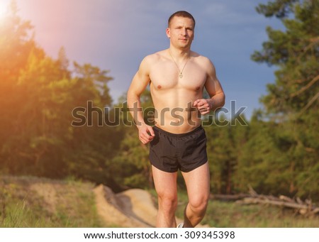 Young muscular man jogging outdoors on a summer evening. The sun\'s rays illuminate the man