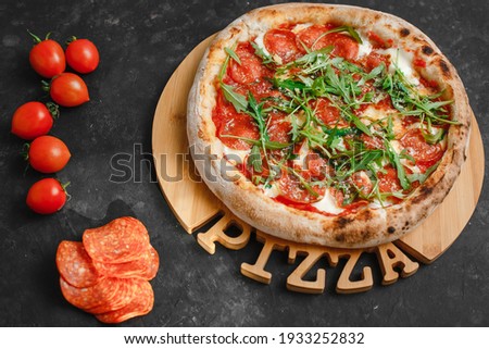Homemade Pepperoni pizza with Mozzarella cheese, salami, tomato sauce, pepper, arugula and spices. Italian pizza on a dark gray black background