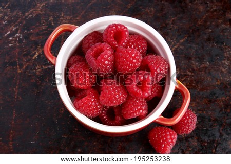 Raspberries in red bowls on brown background