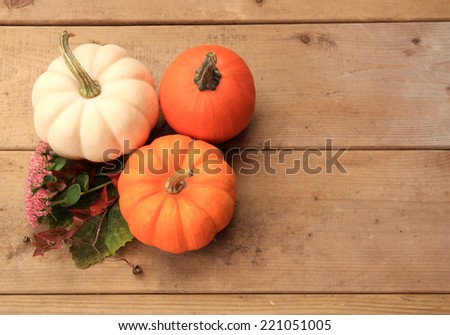 Three pumpkins on wood background with autumn leaves and flowers. Halloween or Thanksgiving decor.