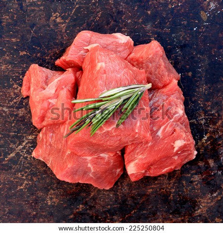 Raw beef cubes with rosemary on brown rustic background