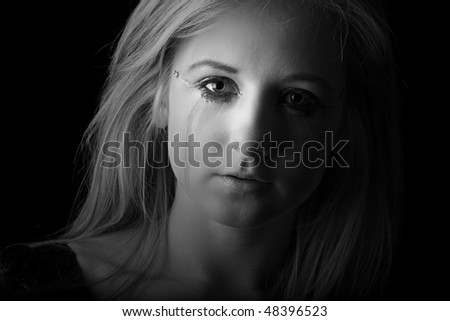 Beautiful Teenage blonde girl in a low key black and white setting crying