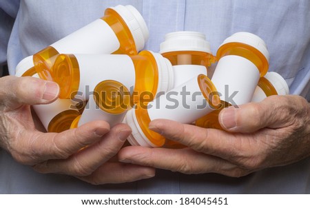 Tight shot of a senior man with rough, dry, hands holding several prescription medication bottles in his hands.