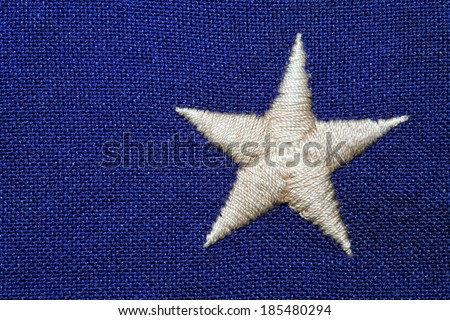 An off white star embroidered on a course weave blue background. This is a detail shot of a USA flag.