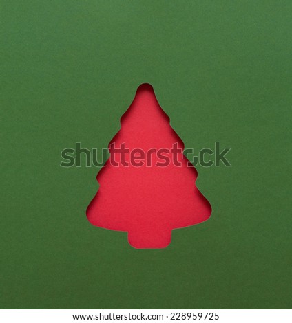 A Christmas tree shape cut into a sheet of green paper floating above a sheet of red.