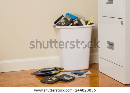 Wastebasket filled with 3.5-inch floppy disks beside a file cabinet.